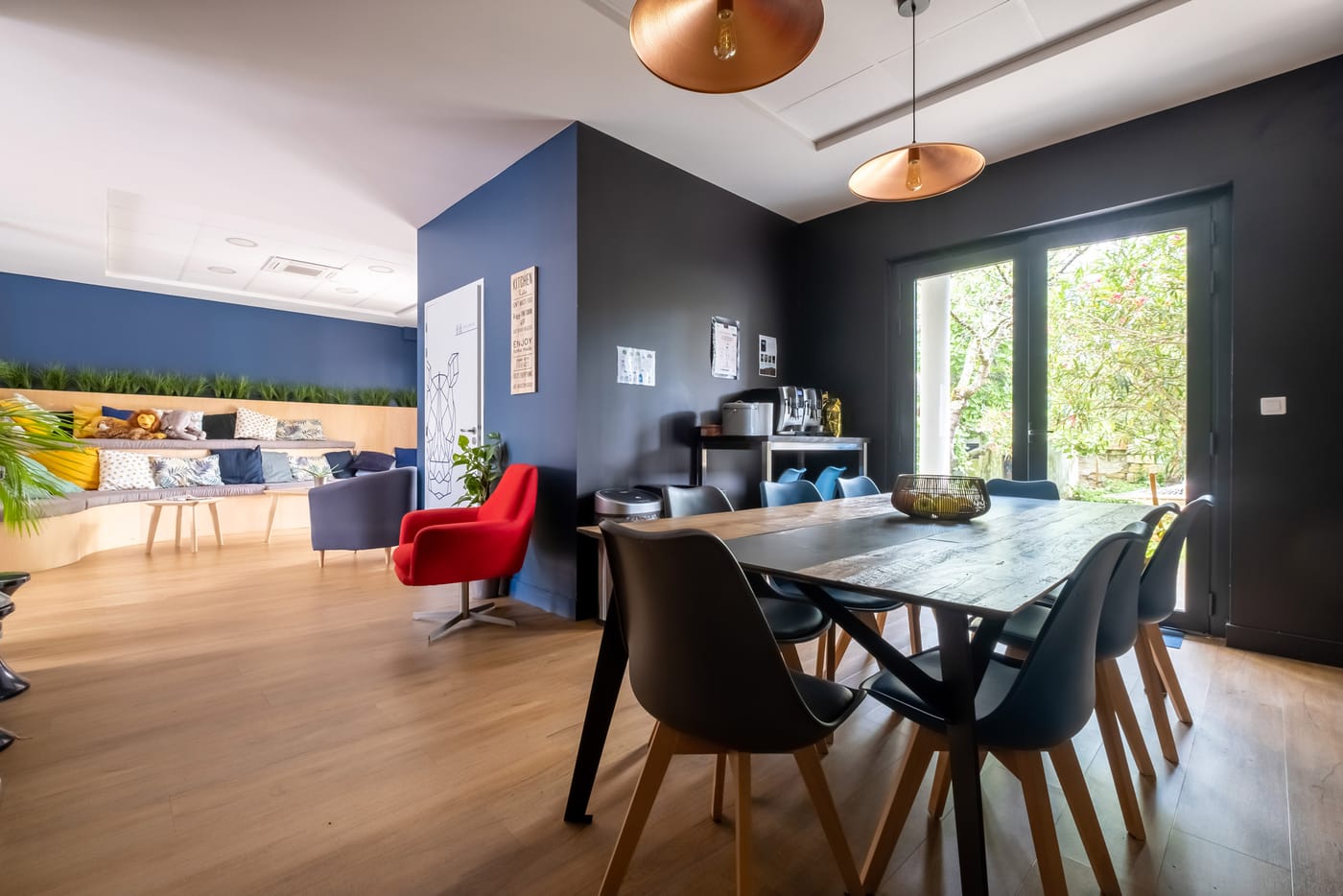 Espace de coworking chaleureux avec grande table en bois, chaises noires et coin salon sur parquet