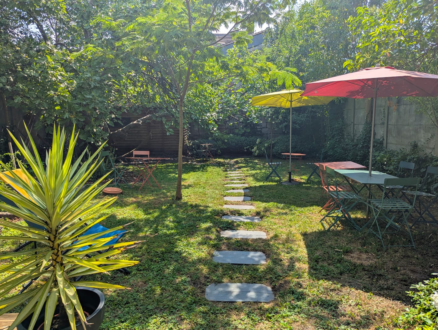 Jardin verdoyant aménagé avec des pas japonais, des parasols et du mobilier de jardin sous les arbres